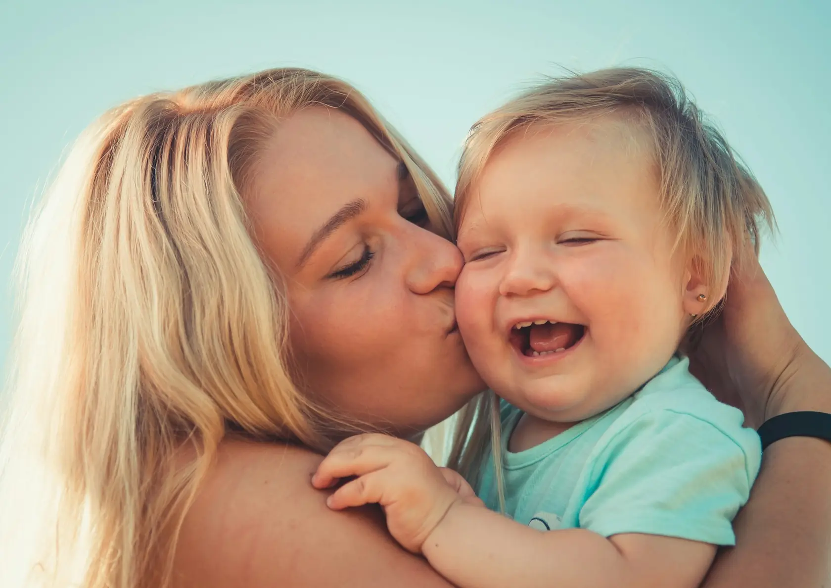 A photograph of a mother kissing her laughing baby, and the pen drawing made from it